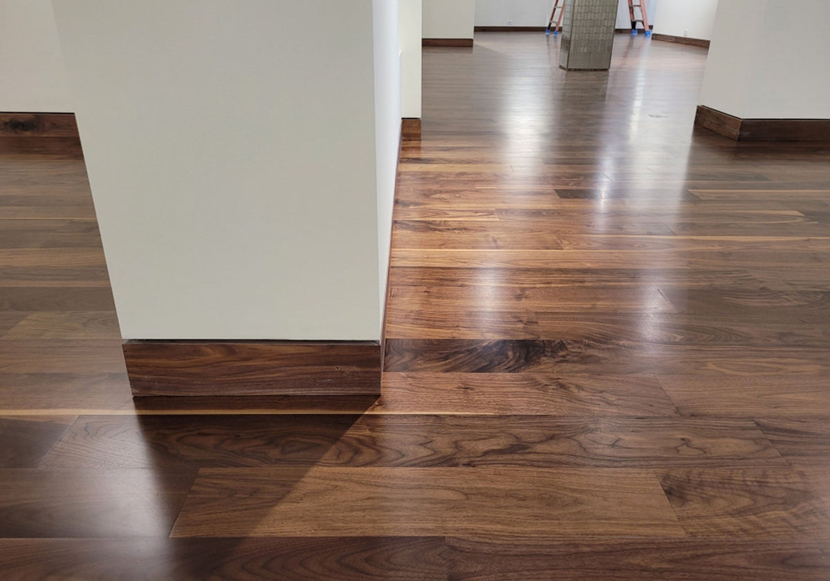 Dark brown hardwood floor with a glossy finish meeting a white wall corner and wood baseboard